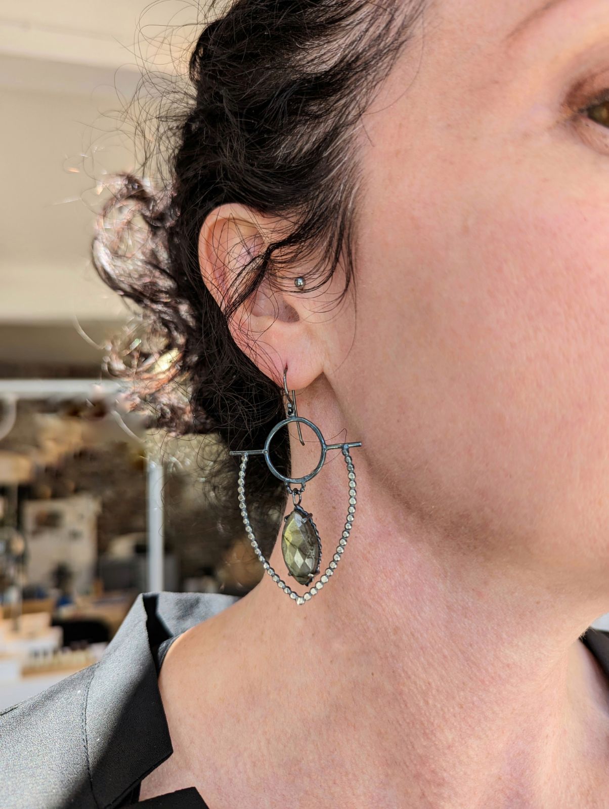dotted blackened silver earrings that look like a shield with marquise green labradorite stones, on model ear by Alice Scott