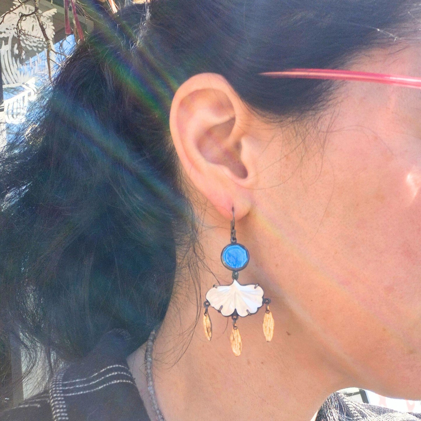 Close-up of an ear wearing a blue and white earring with a blurred background