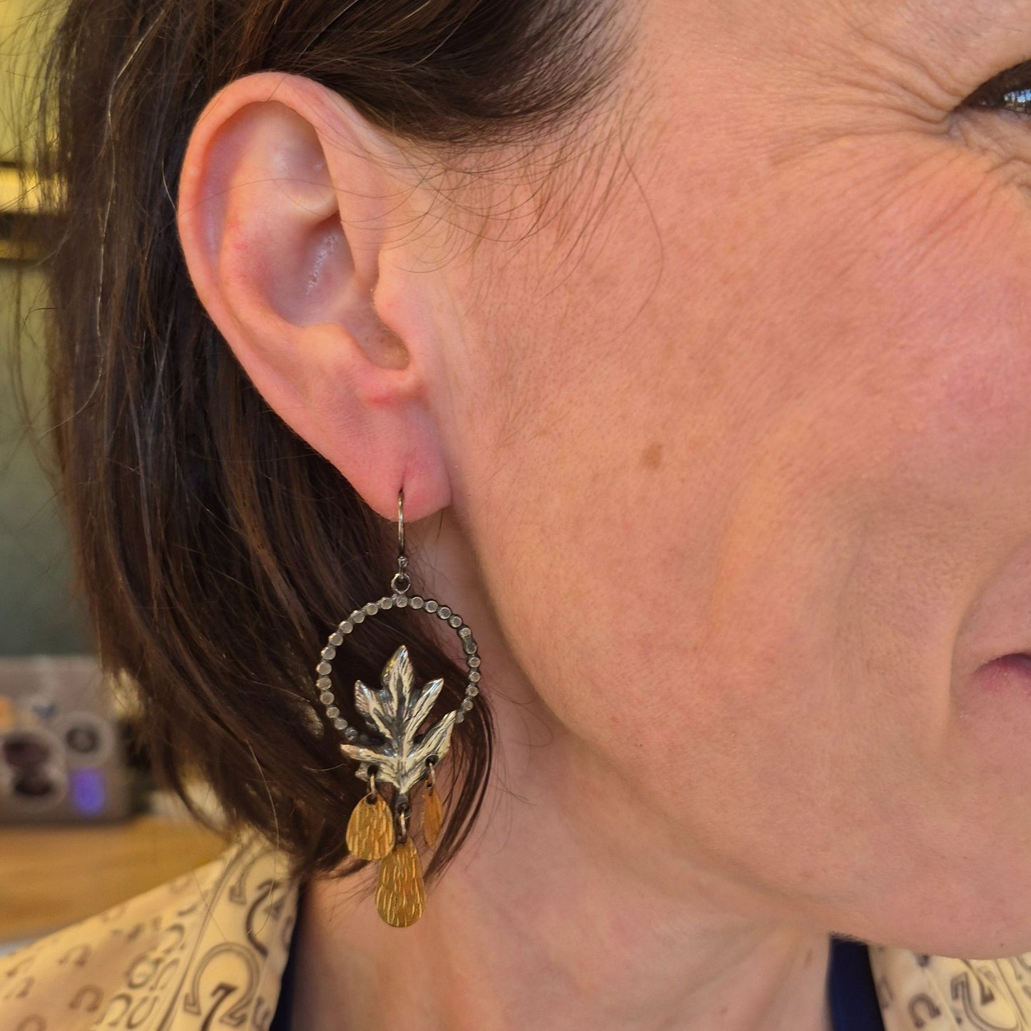 A pair of silver Hawthorn leaf earrings with gold drop accents, displayed on a model by Alice Scott
