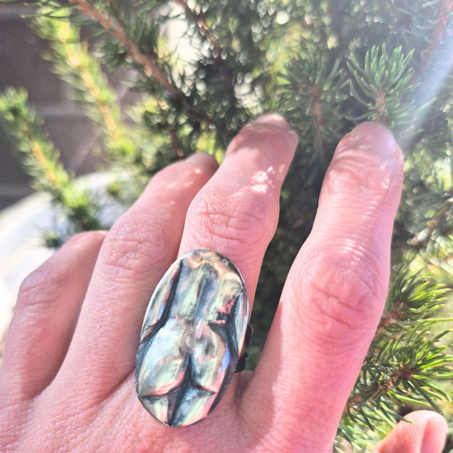 Hand wearing a lady butt ring against a blurred green background by Alice Scott