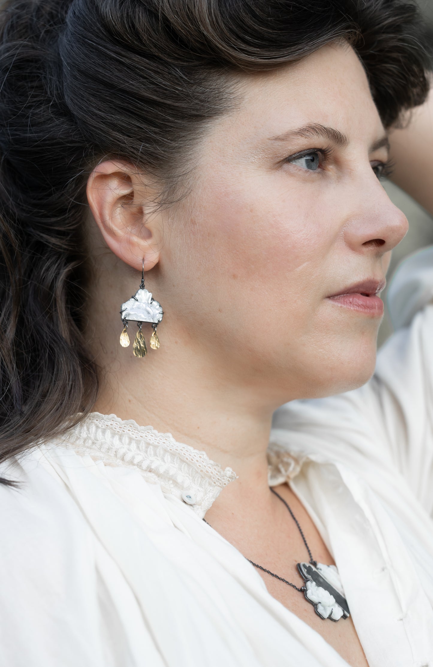 Close-up of a woman wearing A pair of earrings featuring carved mother of pearl flowers with gold fill drops and silver ear wires, by Alice Scott worn on a woman's ears