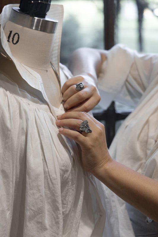 Person adjusting a white dress on a mannequin with a blurred background wearing rings by alice scott