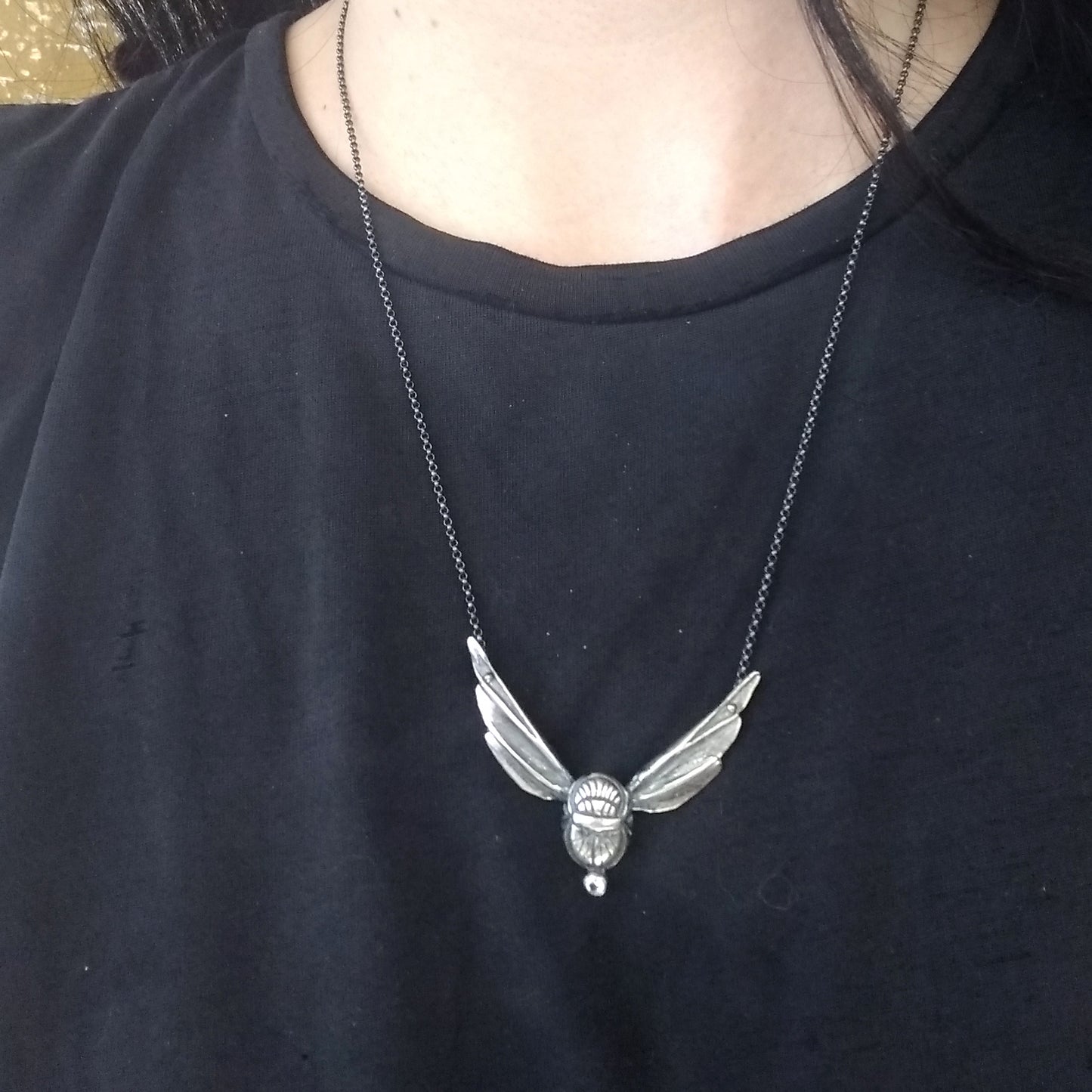A sterling silver scarab wing necklace with a white topaz stone, displayed on a model neck by Alice Scott