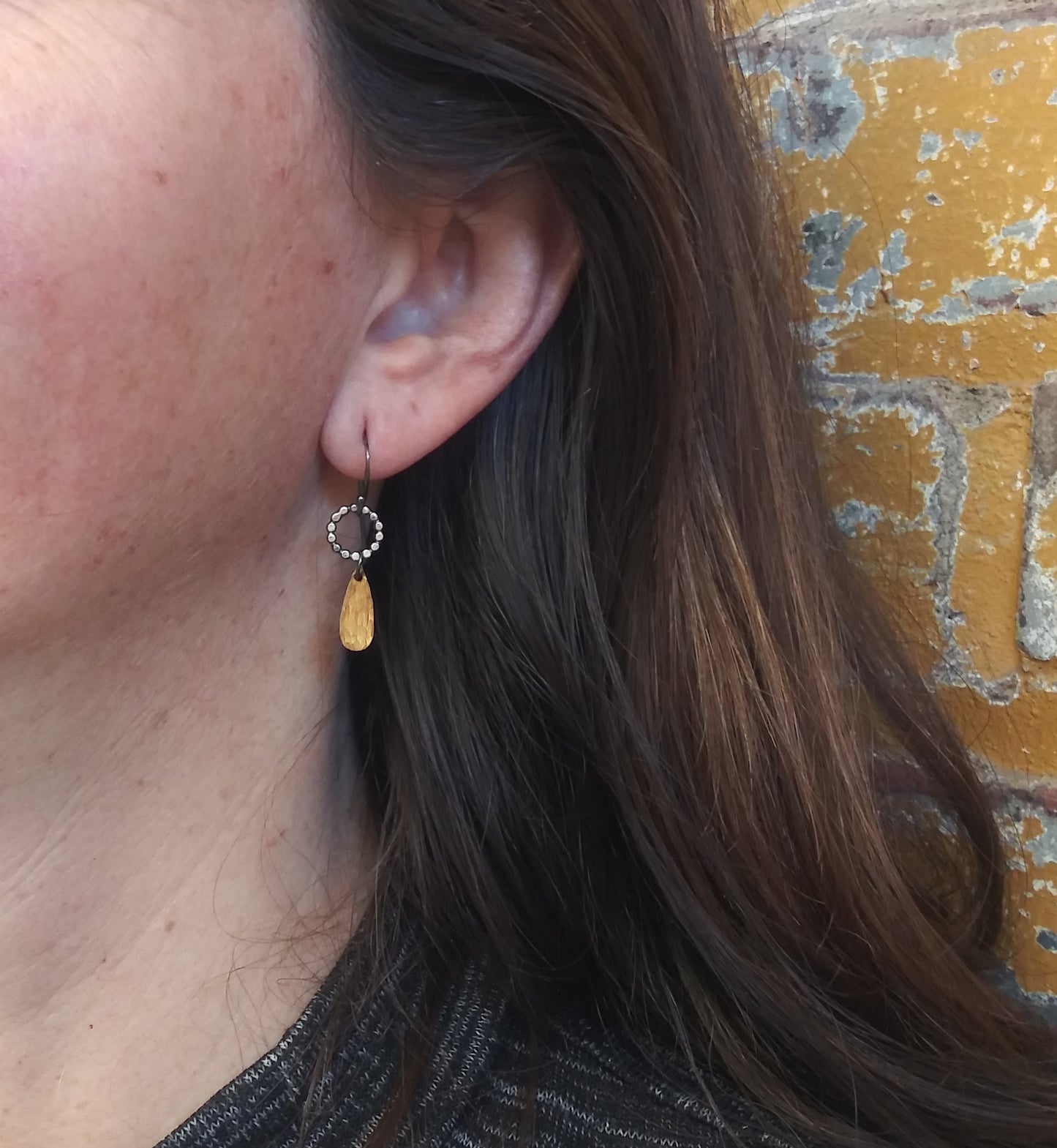 A pair of handmade dangle earrings with gold drops and sterling silver components, displayed on a model ear, by Alice Scott