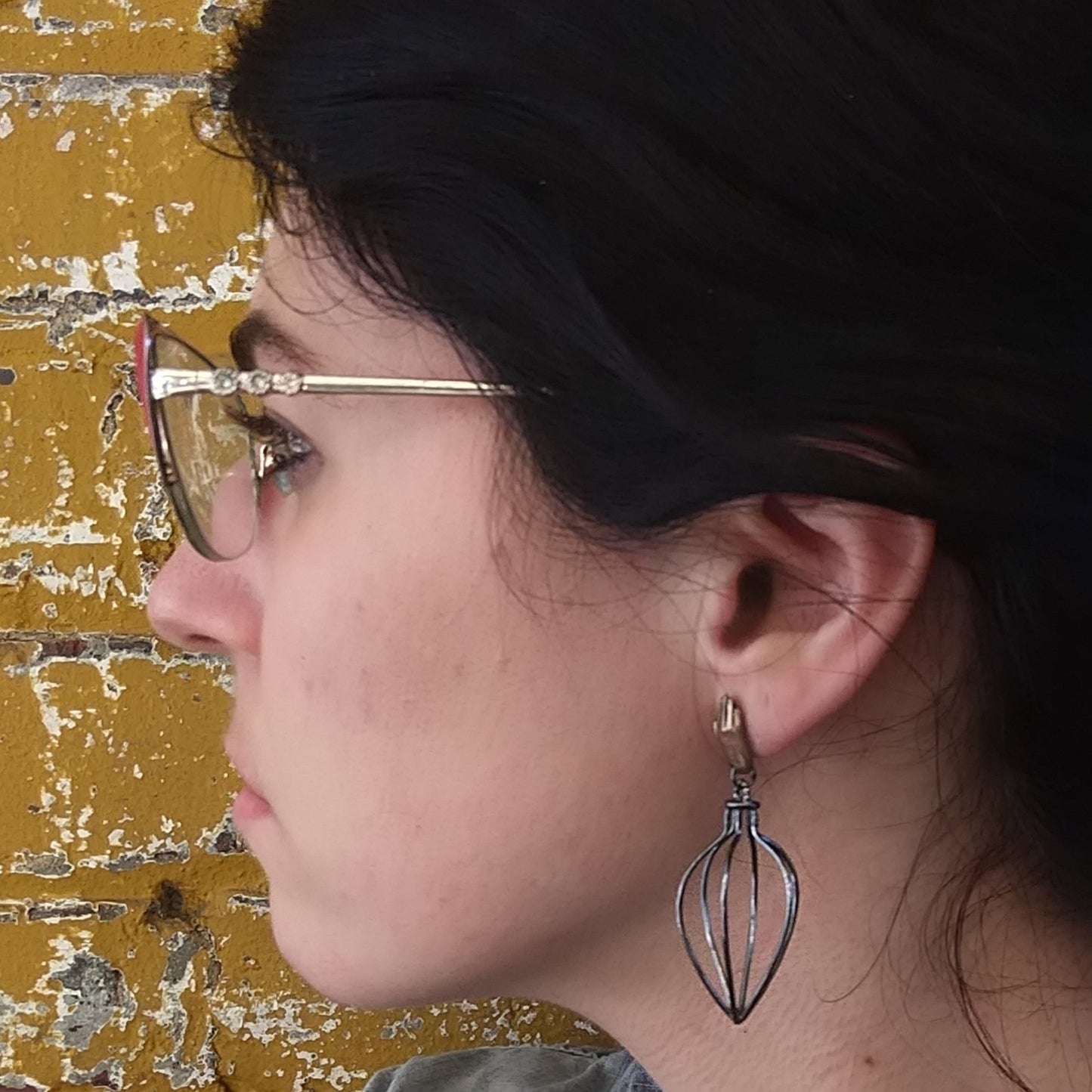 A pair of earrings featuring bronze hands above silver wire vessels with a black patina by Alice Scott