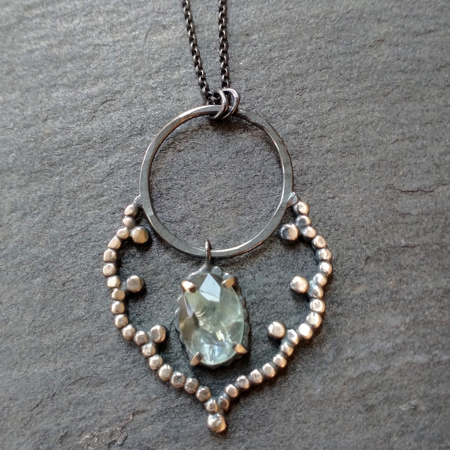 A sterling silver necklace with a lacy cloud-shaped pendant set with an aquamarine stone, displayed against a black background, by Alice Scott