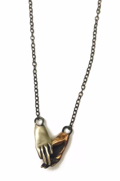A bronze and silver necklace in the shape of two hands holding each other, displayed against a white background, by Alice Scott