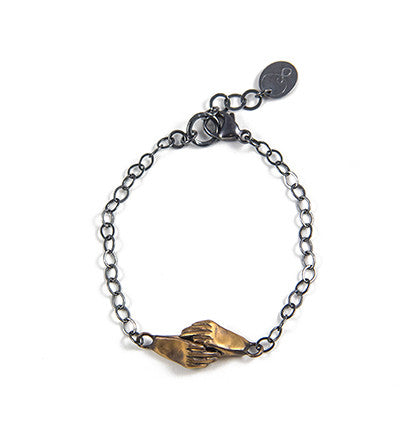 A bronze bracelet featuring a pair of hands holding each other, linked together, with a silver chain and black patina by Alice Scott on white background