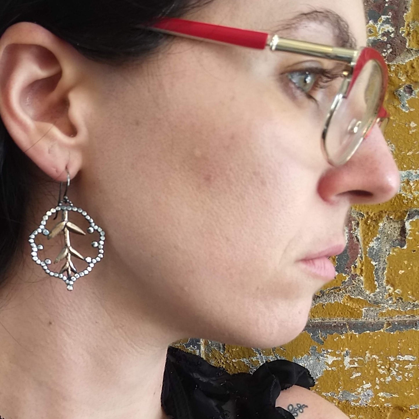 A pair of earrings featuring a lacy cloud design with bronze roots and silver accents on model ear, by Alice Scott