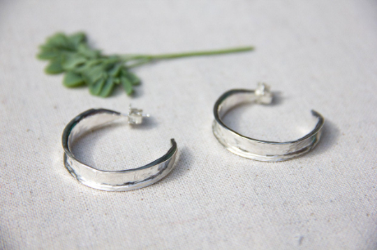 A pair of sterling silver hammered hoop earrings resting on a piece of fabric by Alice Scott