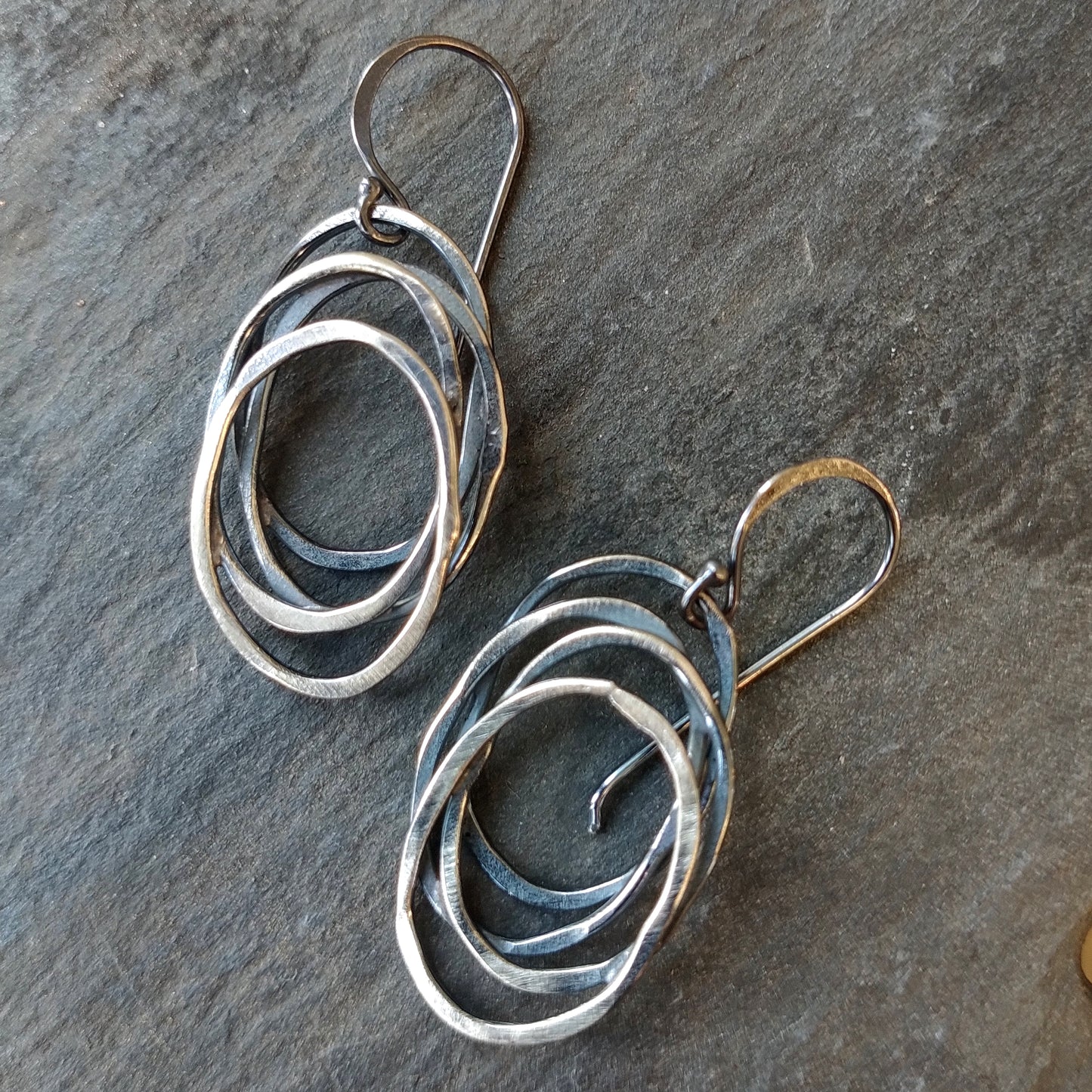 A pair of silver dangle earrings with a galaxy-inspired design, featuring multiple interwoven circles by Alice Scott on a slate background