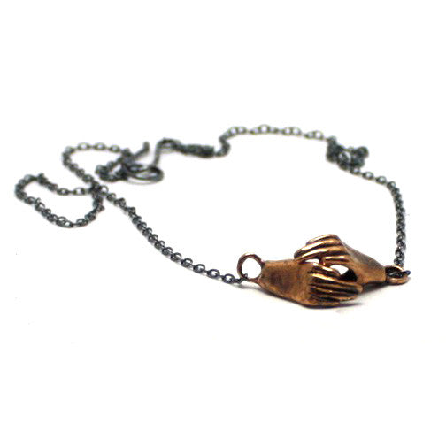 A bronze necklace featuring two hands holding each other, attached to a sterling silver chain with a sterling clasp, by Alice Scott on a white background