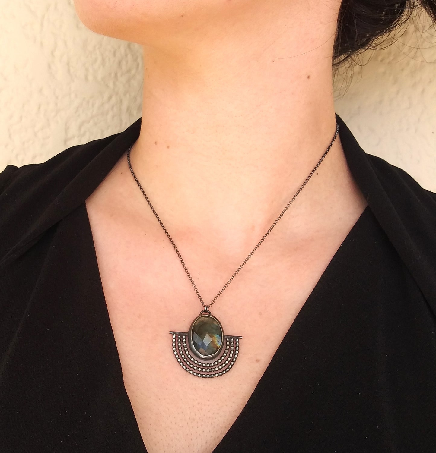 A sterling silver necklace with a black patina featuring an outstretched wing design with a rosecut labradorite gemstone in the center, placed on a model neck by Alice Scott