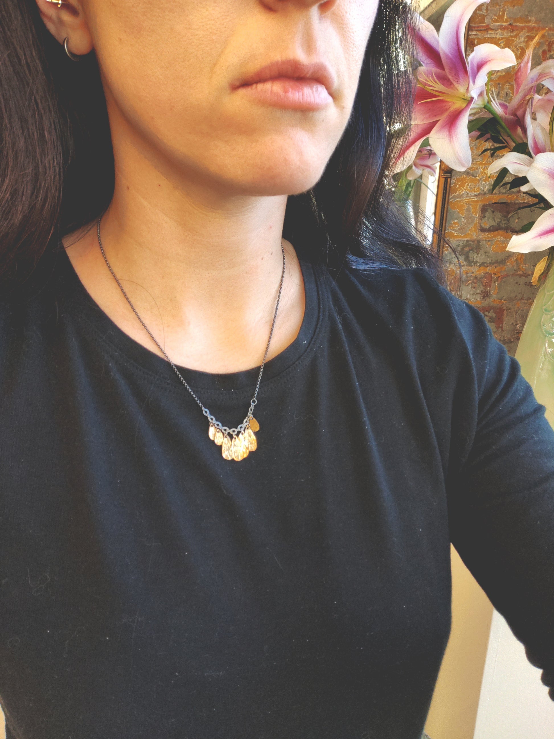 A handmade golden drop cluster necklace with a blackened silver chain by Alice Scott on model neck.