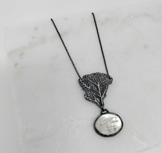 silver necklace with carved mother of pearl moon face and blacked silver yarrow design on a marble background, by Alice Scott