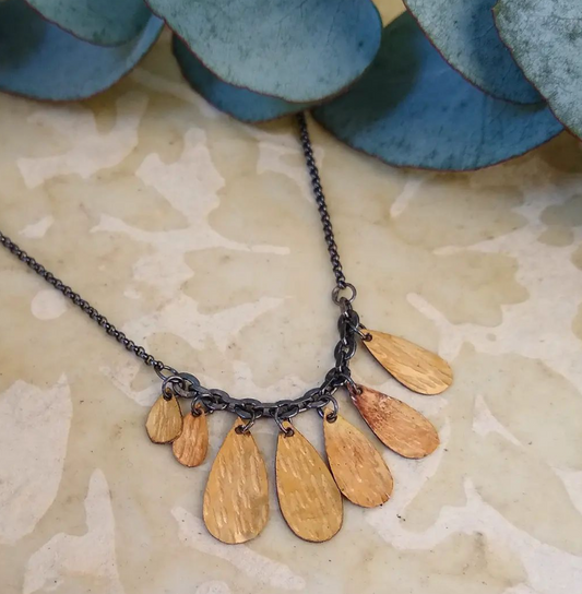 A handmade golden drop cluster necklace with a blackened silver chain by Alice Scott on neutral background.