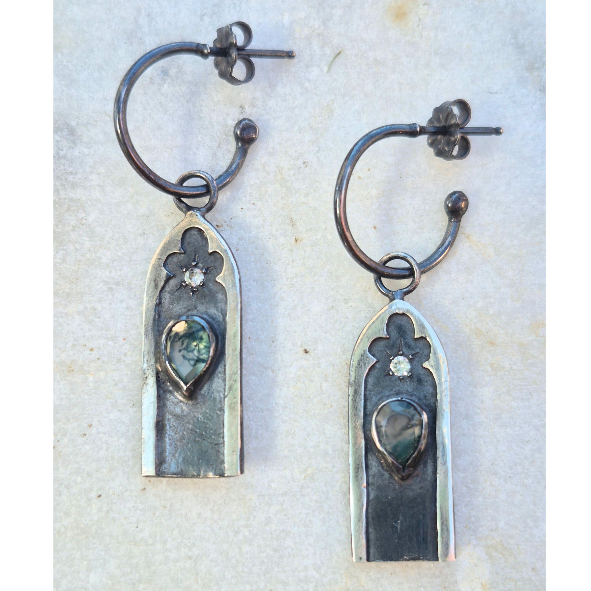 Pair of silver gothic arch earrings with central moss agate gemstones and white sapphire stones on a textured white background by Alice Scott