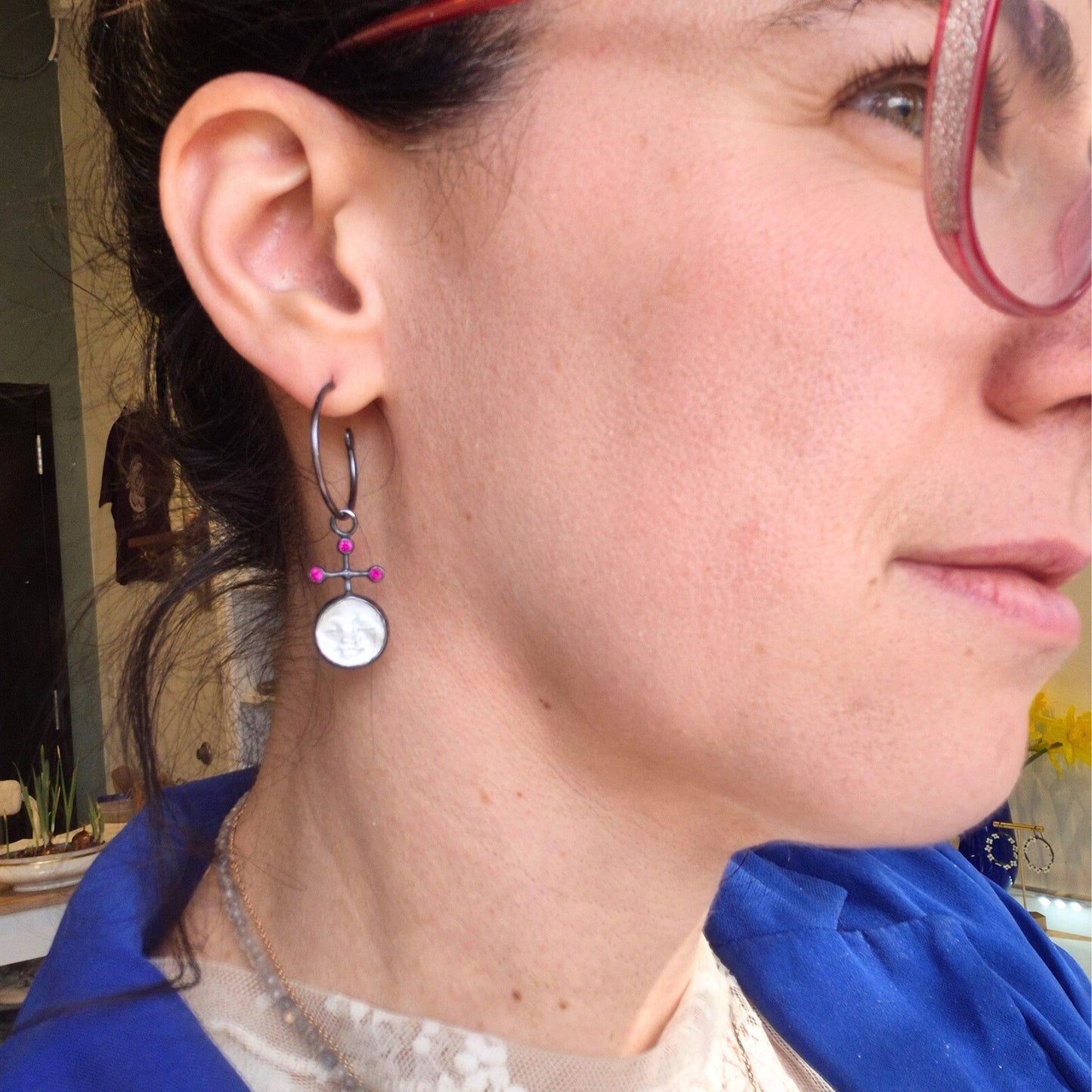 Close-up of a person wearing a hoop earring with a  pearl face and red rubies  with blurred background, by Alice Scott