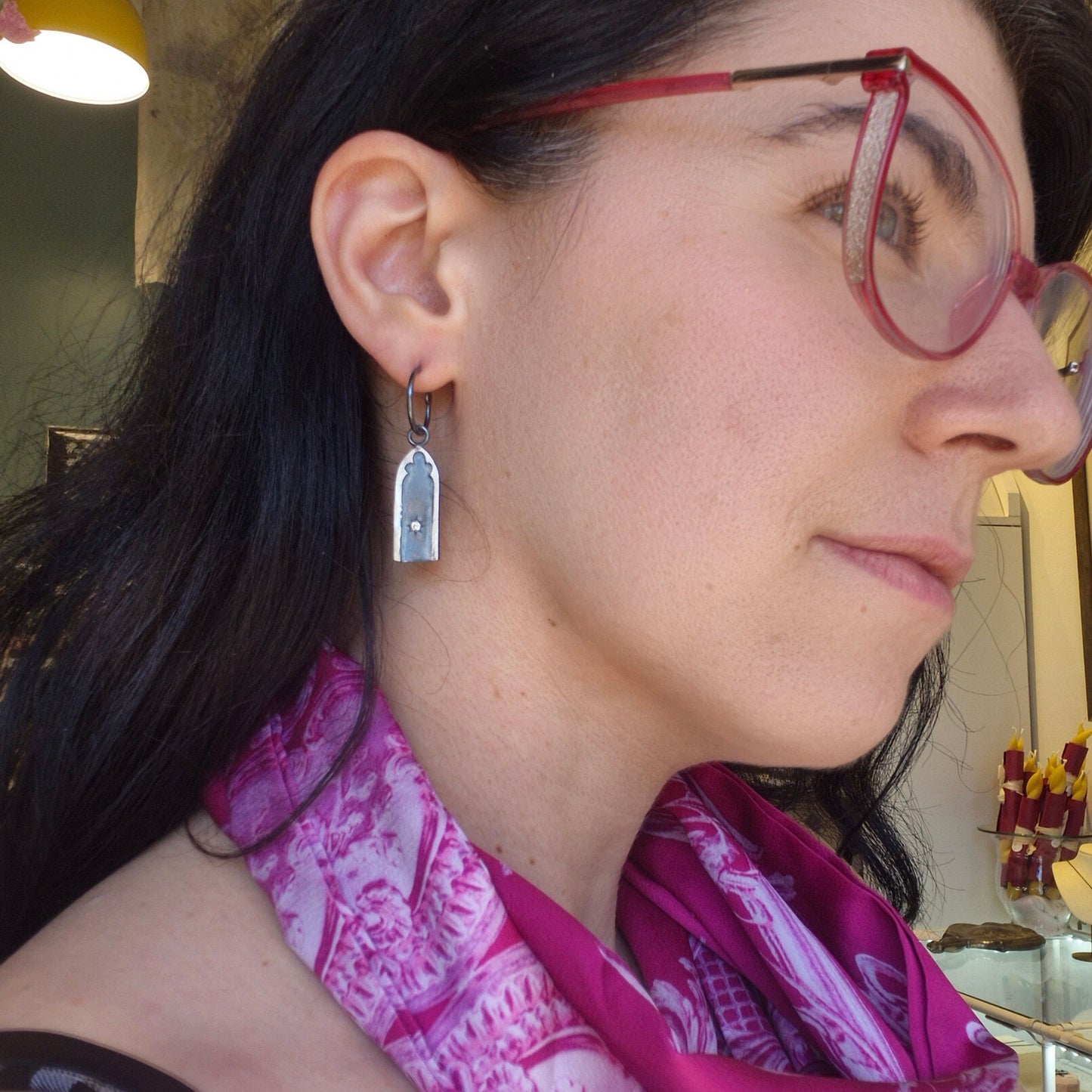Close-up of a woman wearing gothic arch earrings with a blurred indoor background by Alice Scott
