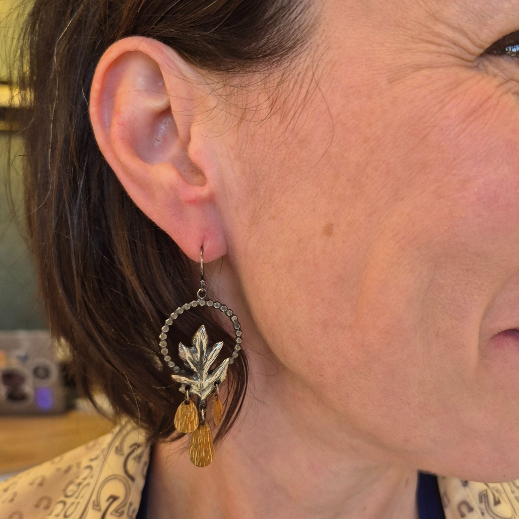 A pair of silver Hawthorn leaf earrings with gold drop accents, displayed on a model  by Alice Scott