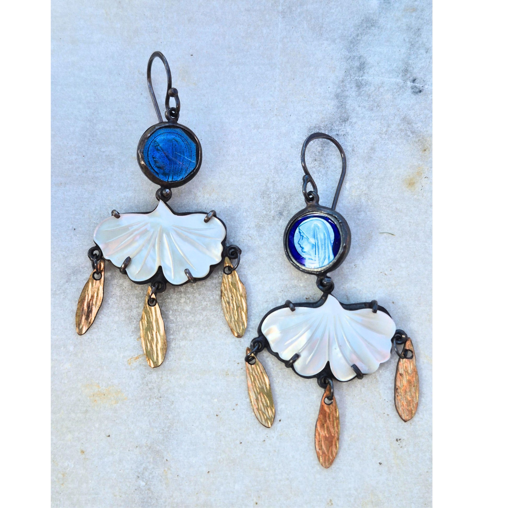 Pair of earrings with mother of pearl shell and vintage rosaries on a textured surface by Alice Scott