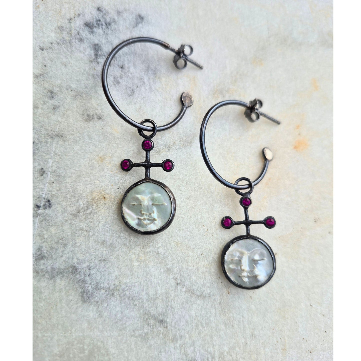 Pair of hoop earrings with circular pearl face charms and red ruby stones on a textured surface by Alice Scott
