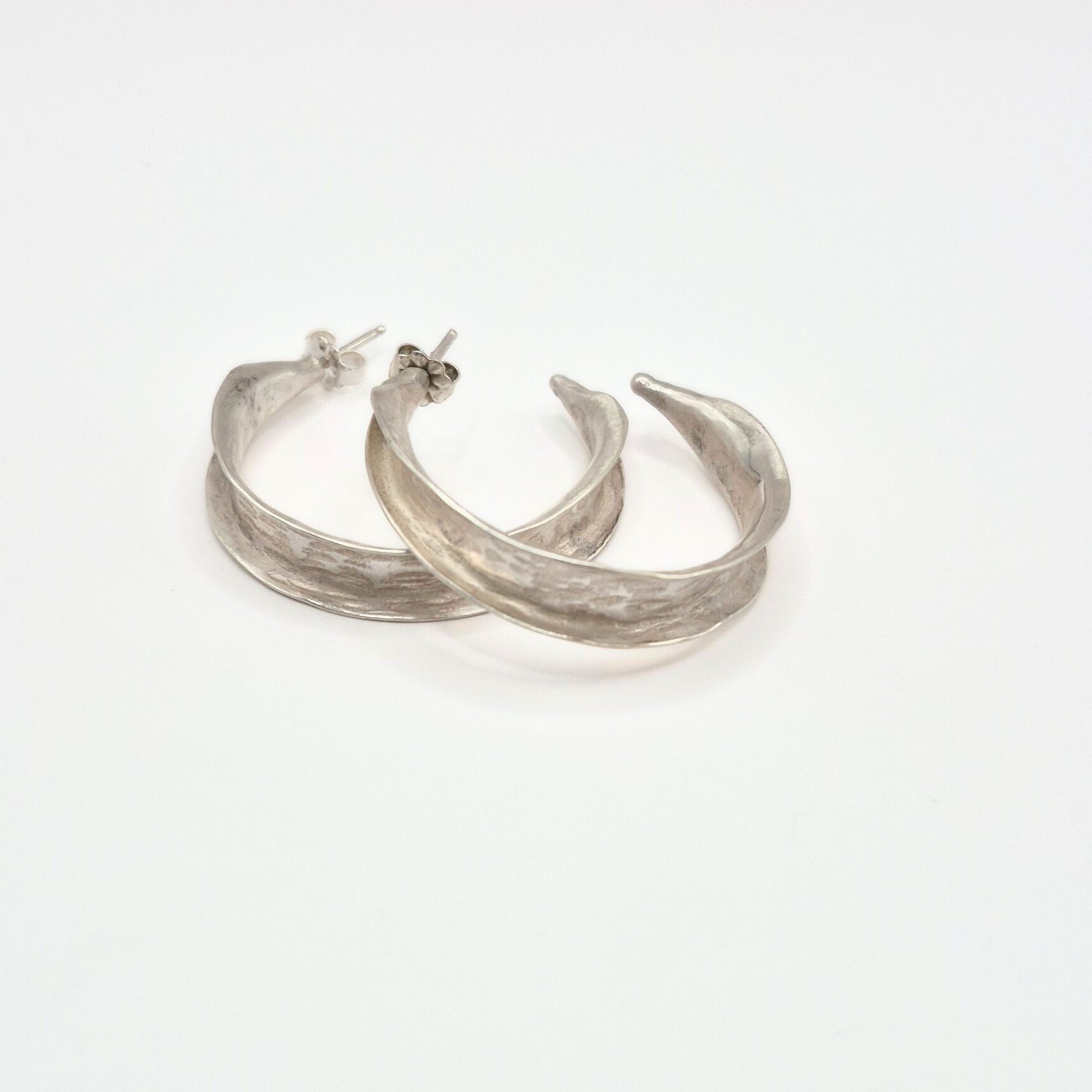 A pair of sterling silver hammered hoop earrings resting on a white background by Alice Scott