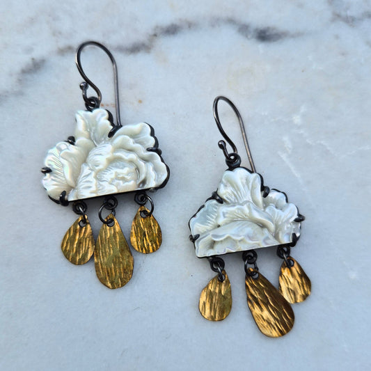 A pair of earrings featuring carved mother of pearl flowers with gold fill drops and silver ear wires, displayed on a marble surface by Alice Scott