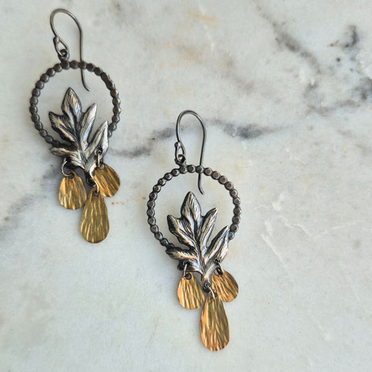 A pair of silver Hawthorn leaf earrings with gold drop accents, displayed on a marble surface by Alice Scott