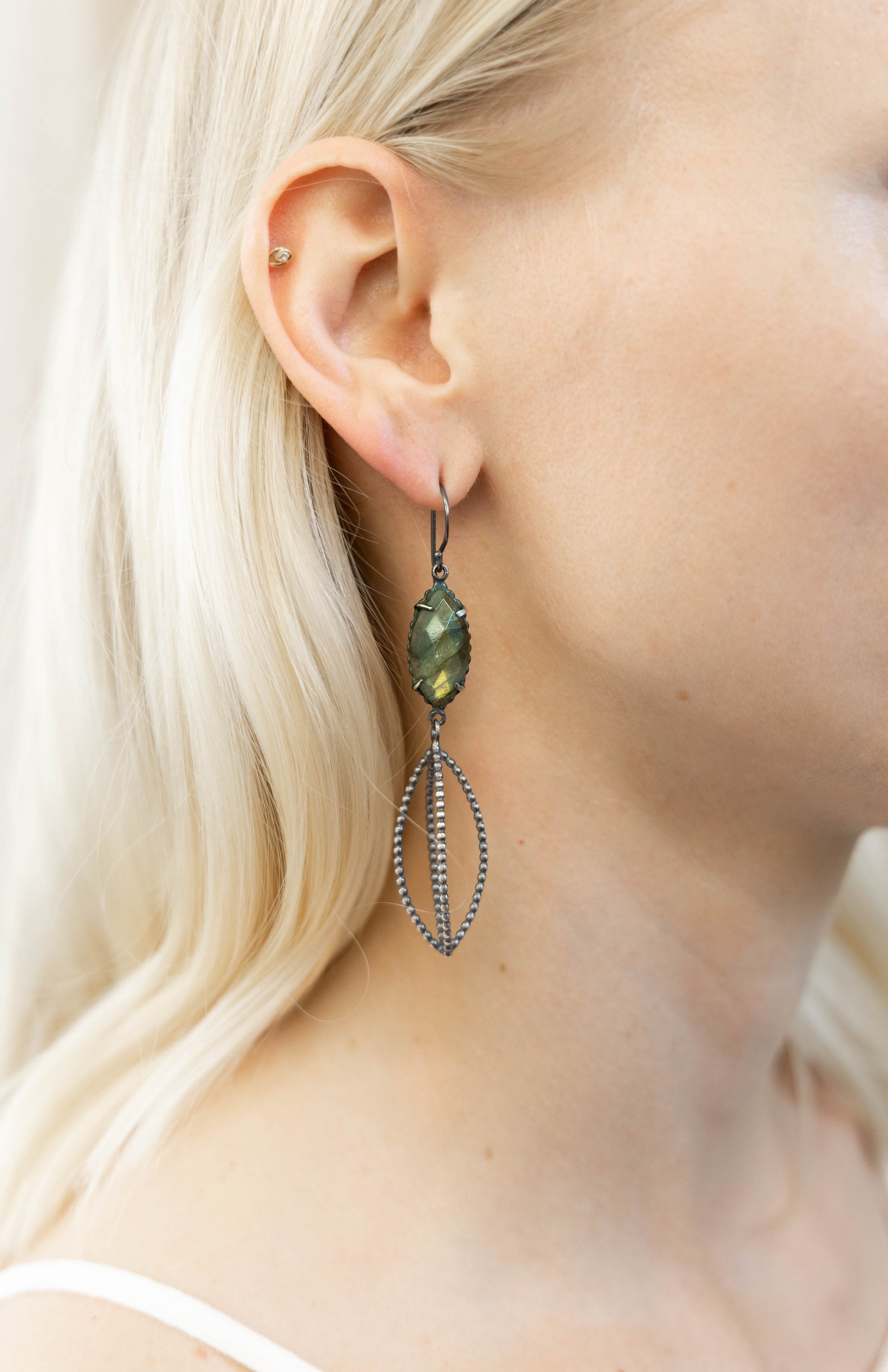 A pair of dangle earrings featuring natural labradorite stones with a silver dotted cage below captured on a model by Alice Scott