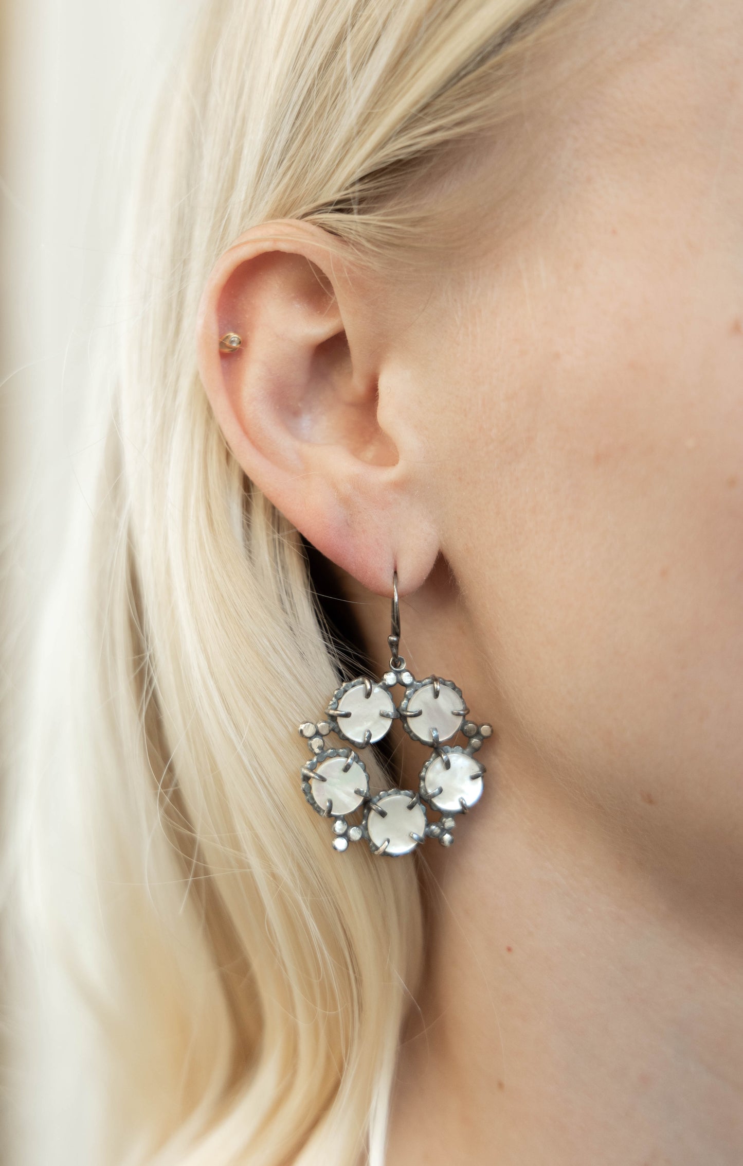 A pair of silver, mother of pearl earrings with a star and constellation design, displayed against a model ear by Alice Scott