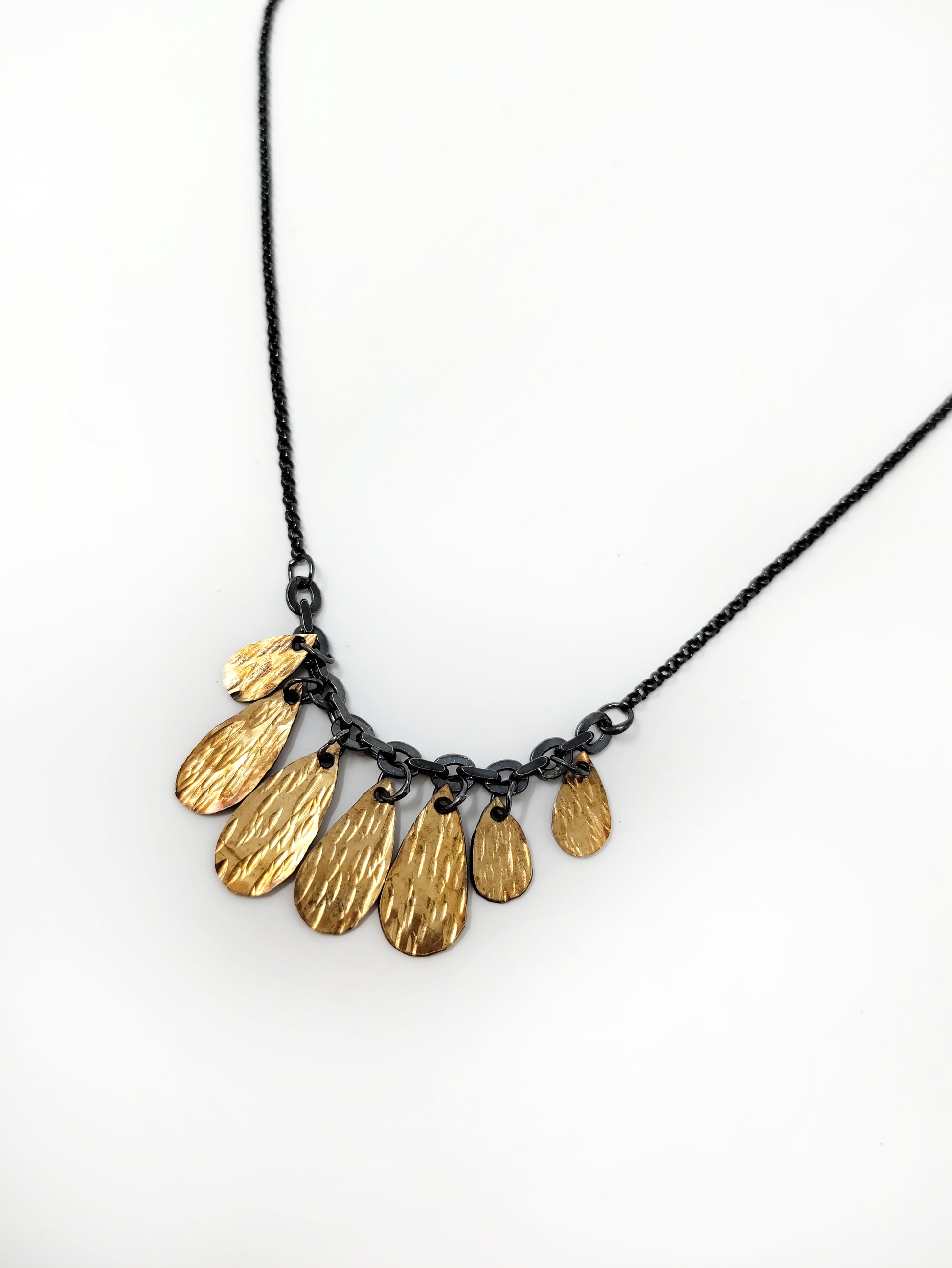 A handmade golden drop cluster necklace with a blackened silver chain by Alice Scott on white background.