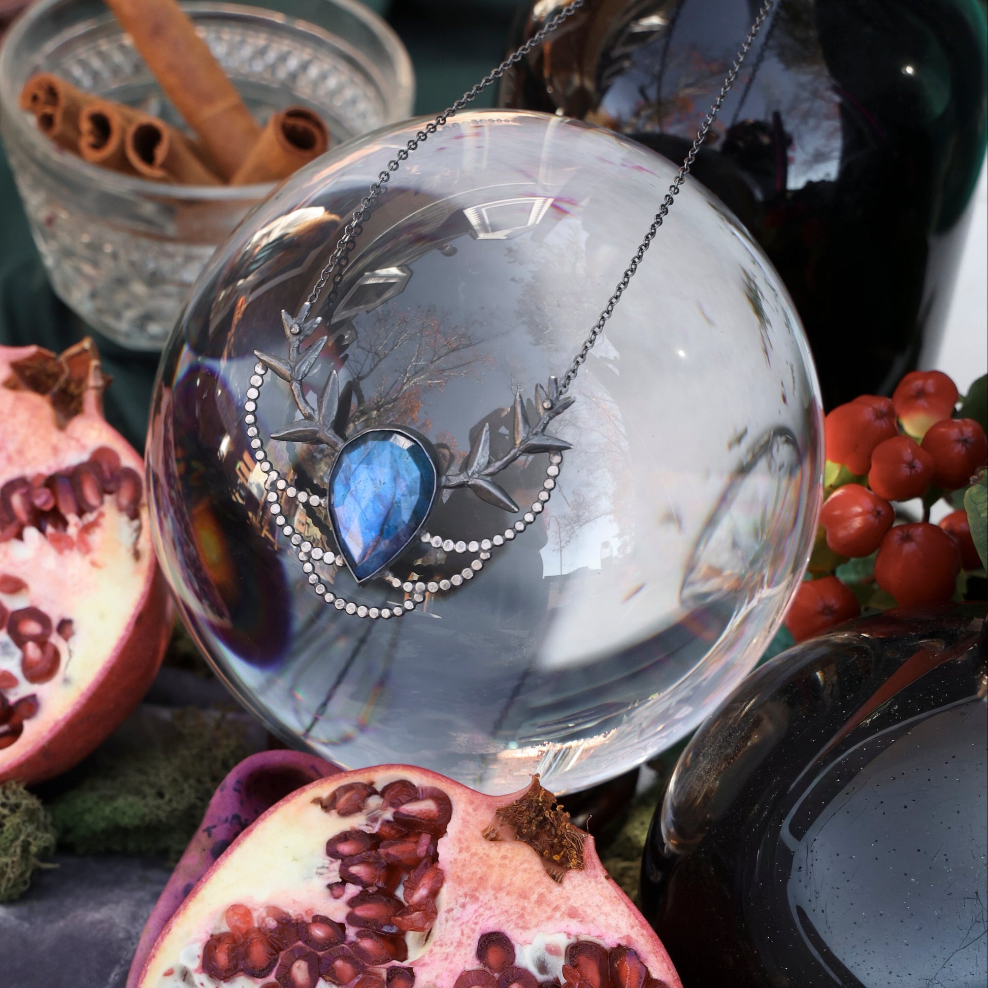 Pomegranate halves on a dark surface with a crystal ball and cinnamon sticks.