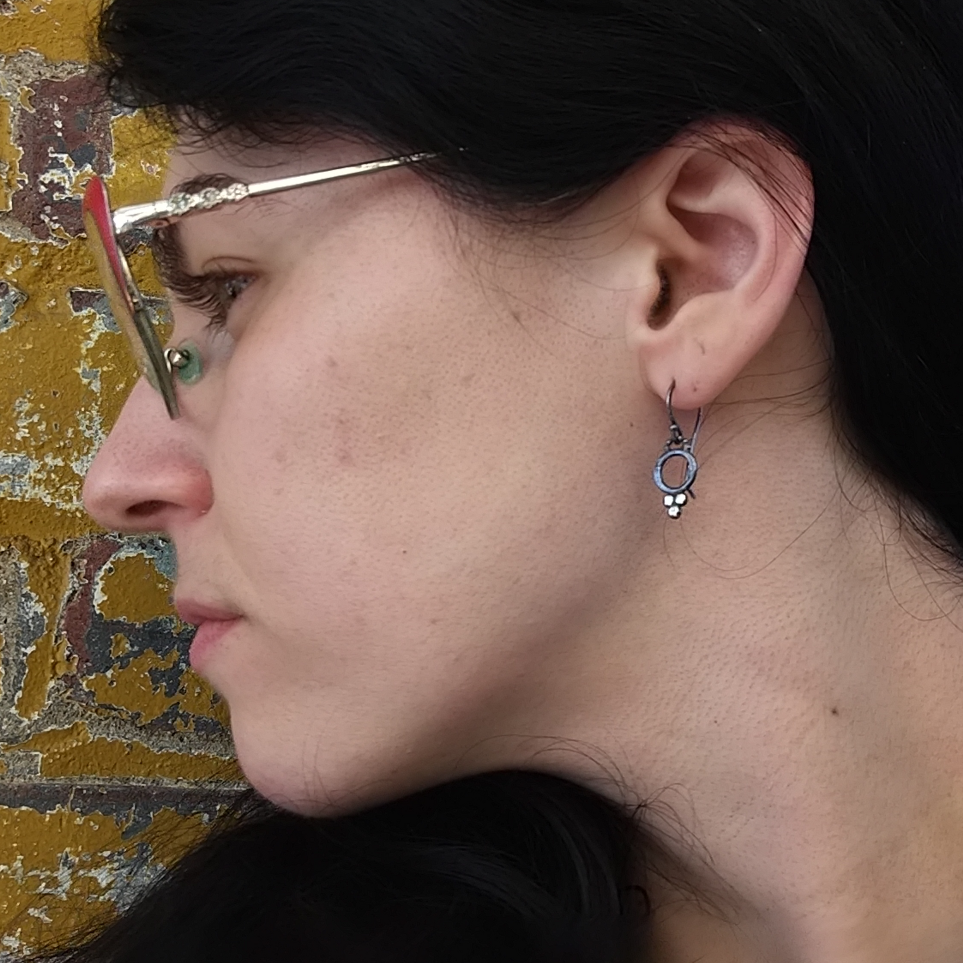 A pair of sterling silver dotted earrings with black patina and silver ear wires, displayed on a model ear by Alice Scott
