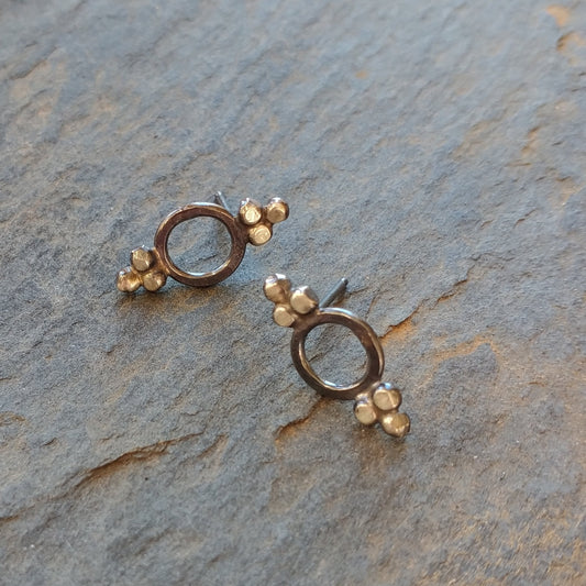 A pair of Victorian-style stud earrings with blackened sterling silver dots and circular inside, displayed on a textured surface, by Alice Scott