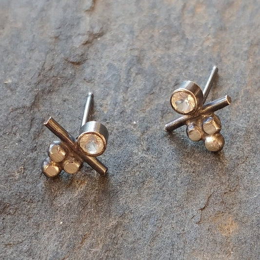 A pair of silver stud earrings with white topaz stones, displayed on a textured surface, by Alice Scott
