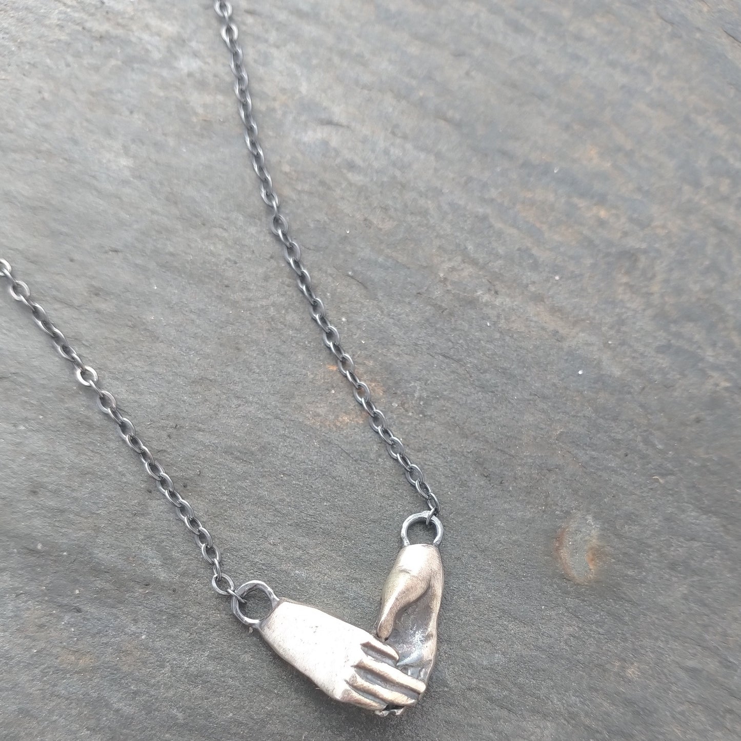 A sterling silver necklace featuring two hands in a hugging gesture, attached to a chain, by Alice Scott