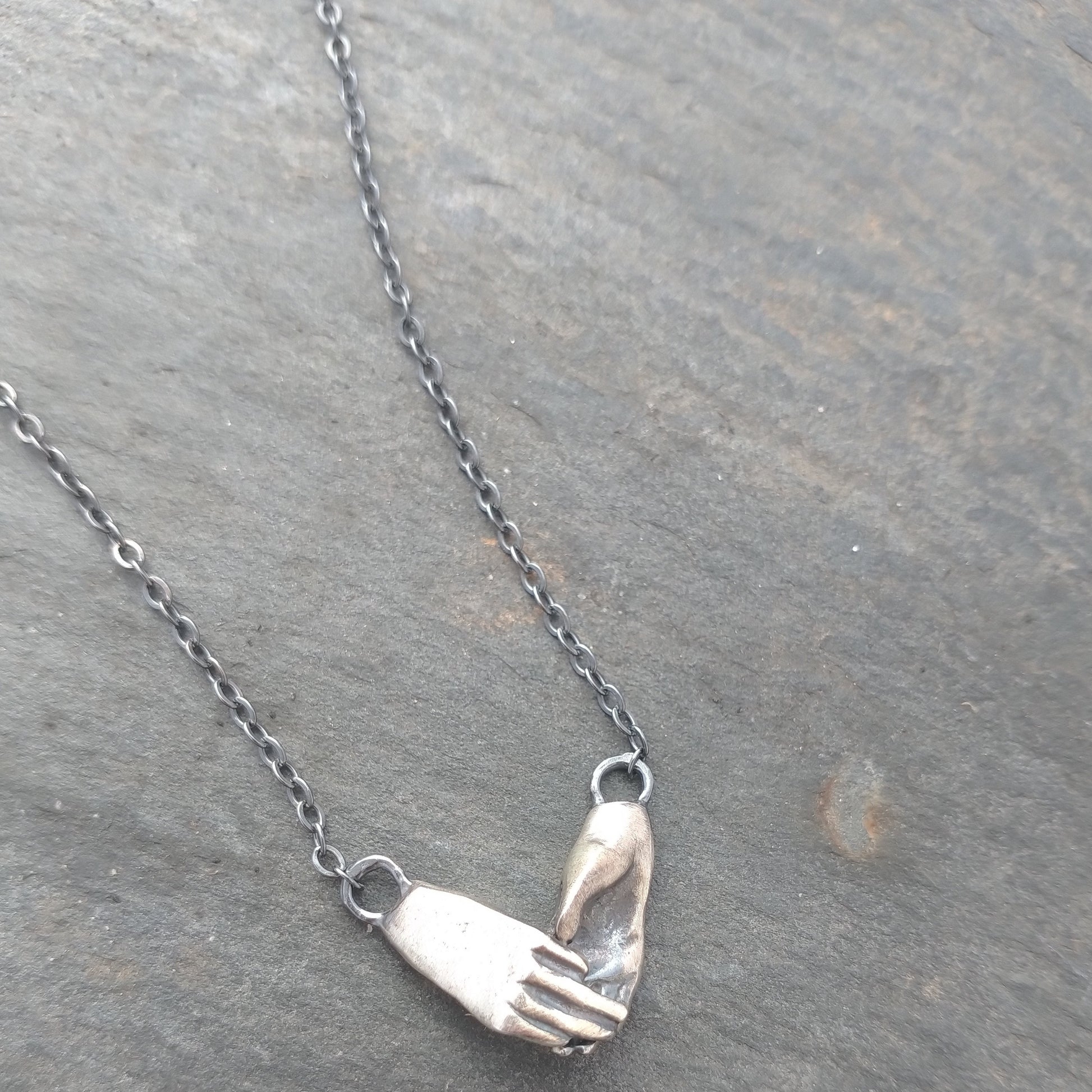 A sterling silver necklace featuring two hands in a hugging gesture, attached to a chain, by Alice Scott