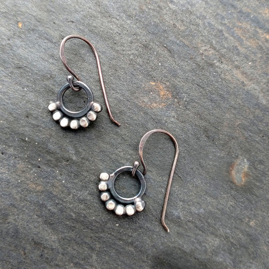 silver dot earrings around a circle in the middle, by Alice Scott, on a grey background