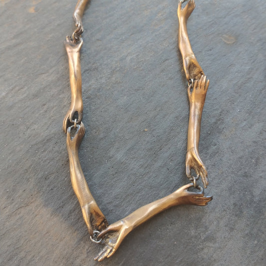 A necklace with bronze hand-shaped links connected by silver rings, withon a blackened silver chain by Alice Scott on grey background