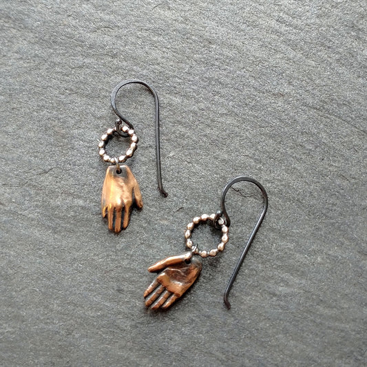bronze hand earrings with silver circles on top, by Alice Scott on slate background