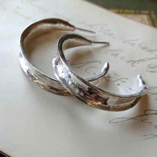 A pair of sterling silver hammered hoop earrings resting on a piece of paper with writing, by Alice Scott