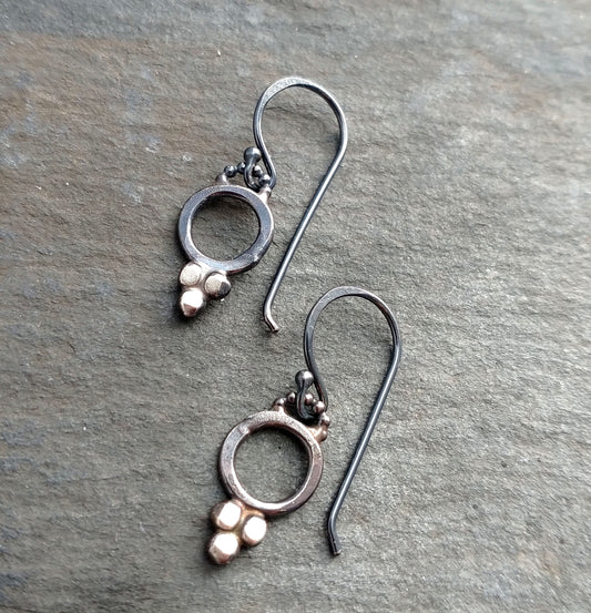 A pair of sterling silver dotted earrings with black patina and silver ear wires, displayed on a textured surface by Alice Scott