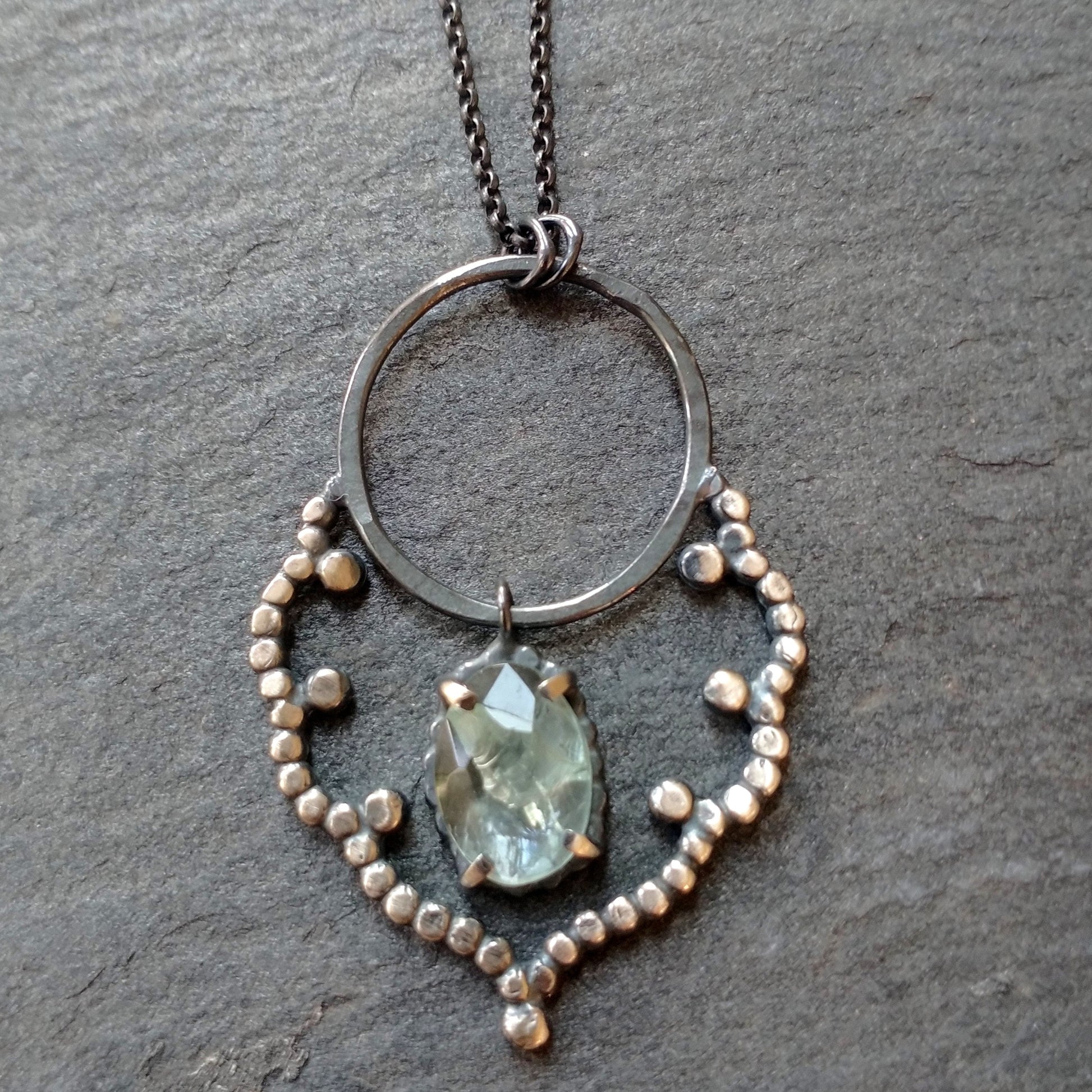 A sterling silver necklace with a lacy cloud-shaped pendant set with an aquamarine stone, displayed against a black background, by Alice Scott