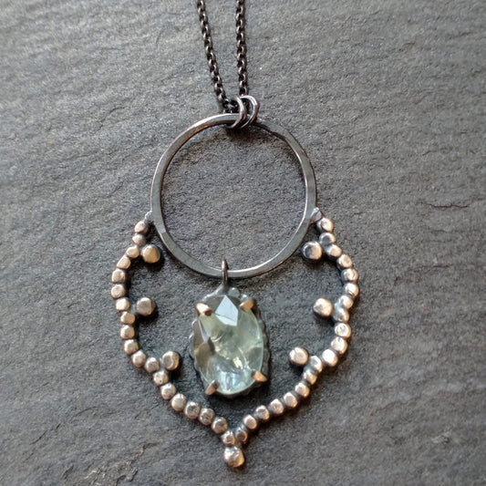 A sterling silver necklace with a lacy cloud-shaped pendant set with an aquamarine stone, displayed against a black background, by Alice Scott