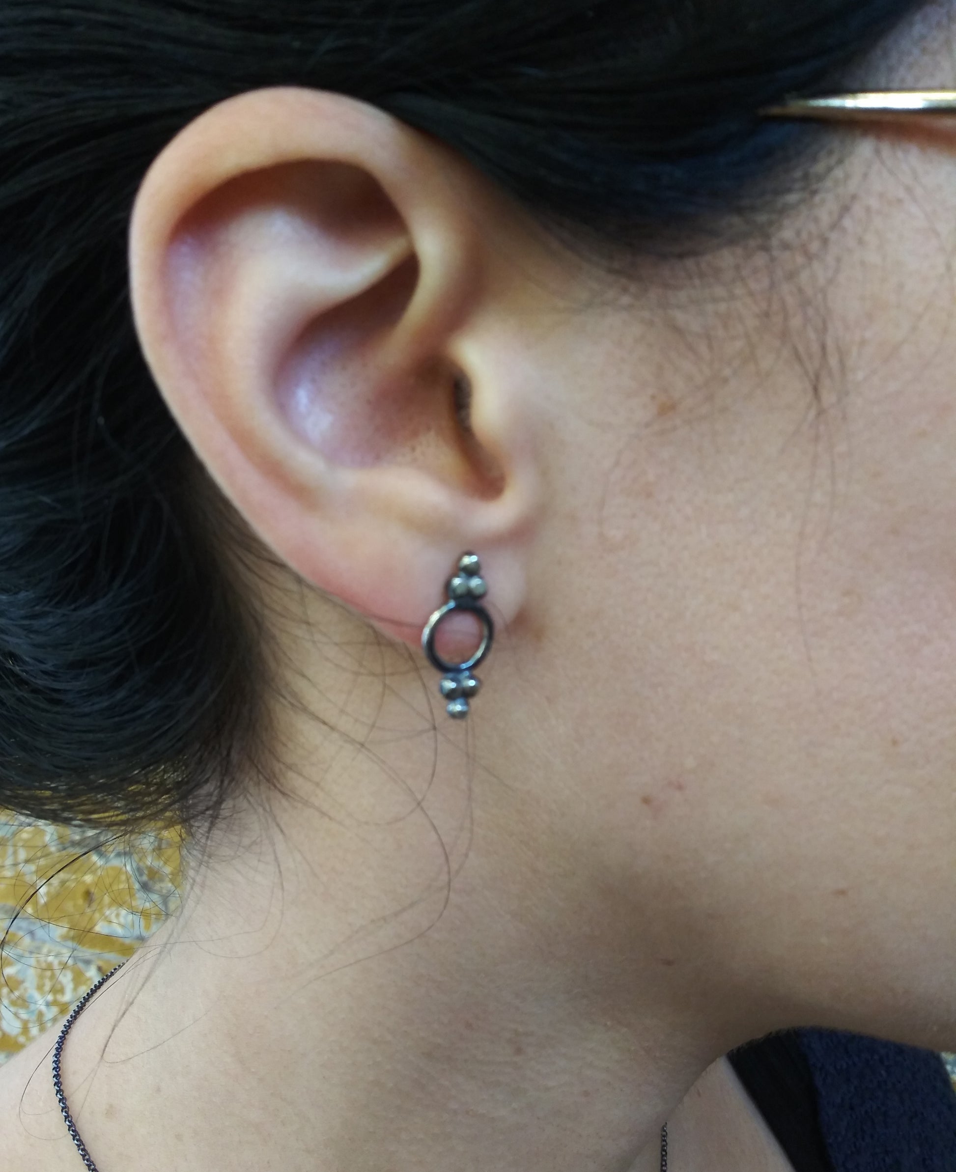 A pair of Victorian-style stud earrings with blackened sterling silver dots and circular inside, displayed on a textured surface, by Alice Scott