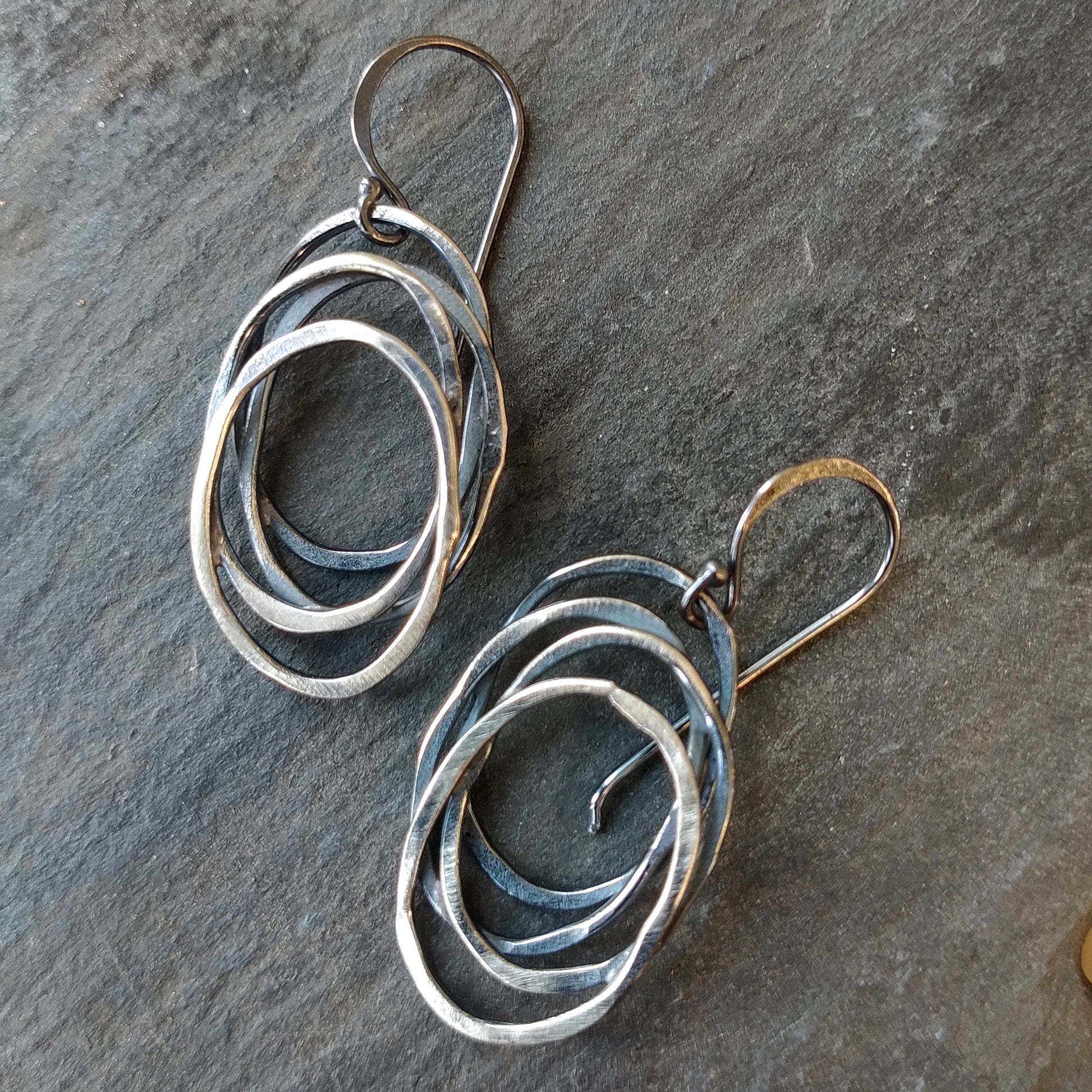 A pair of silver dangle earrings with a galaxy-inspired design, featuring multiple interwoven circles by Alice Scott on a slate background