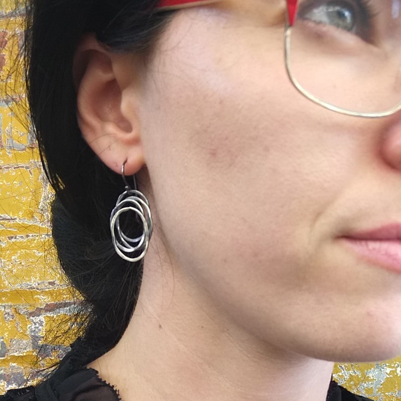 A pair of silver dangle earrings with a galaxy-inspired design, featuring multiple interwoven circles by Alice Scott on a model ear