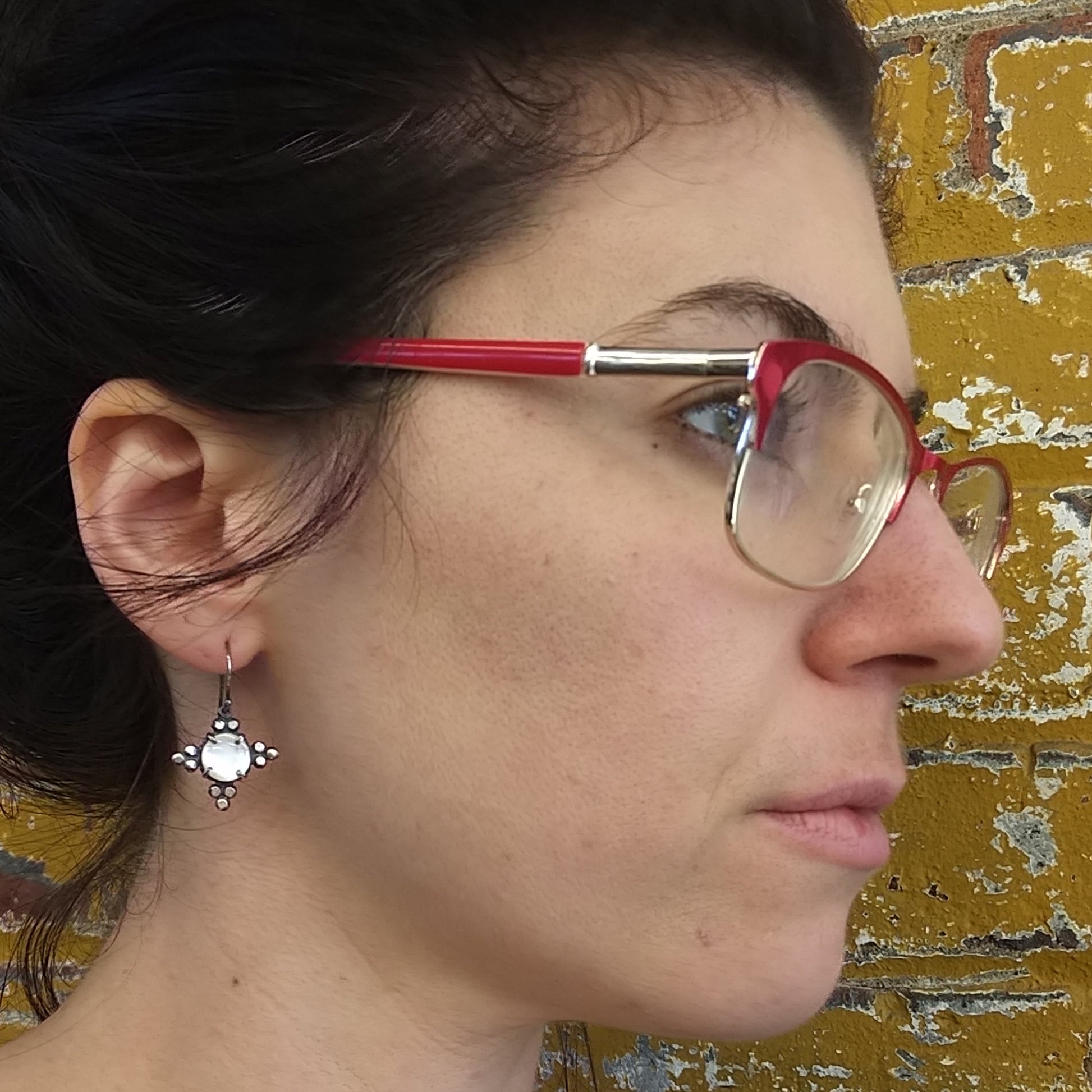 A pair of silver earrings with mother of pearl details, displayed on a model, by Alice Scott.