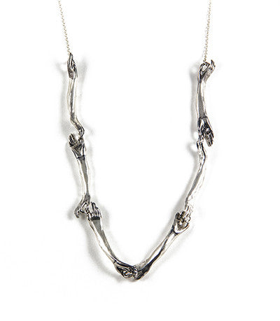 A silver necklace with a unique design featuring hand-shaped links connected by silver rings on a silver chain, by Alice Scott, on white  background.